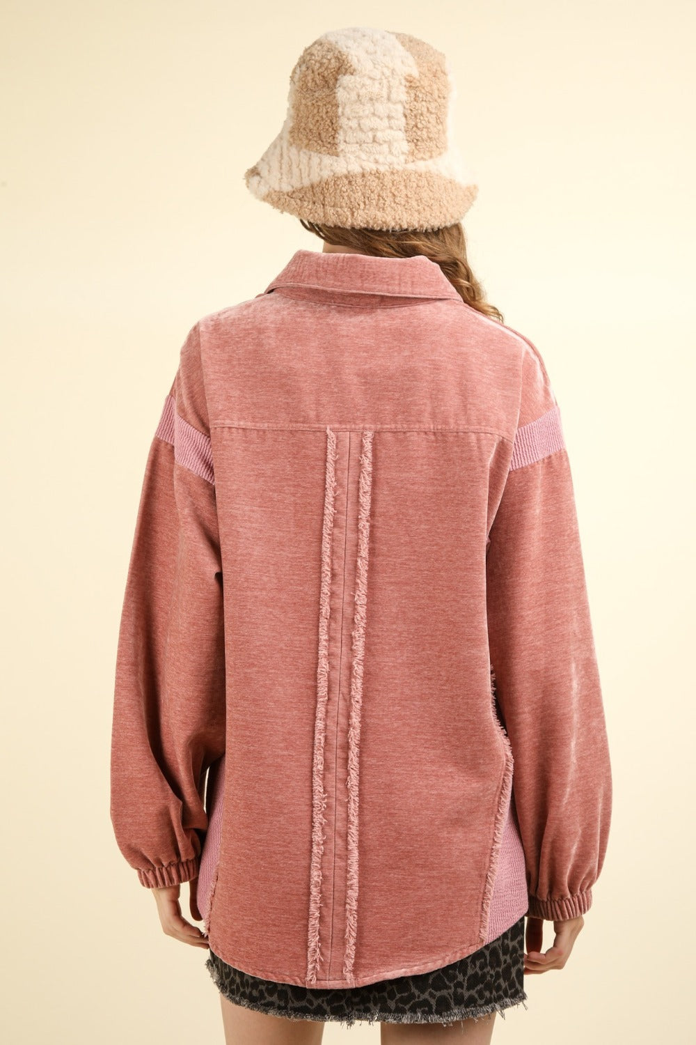 A person showcasing the VERY J Mixed Media Button Down Raw Hem Shacket in pink, paired with a black patterned skirt with a raw hem and a beige hat, stands against a light background.