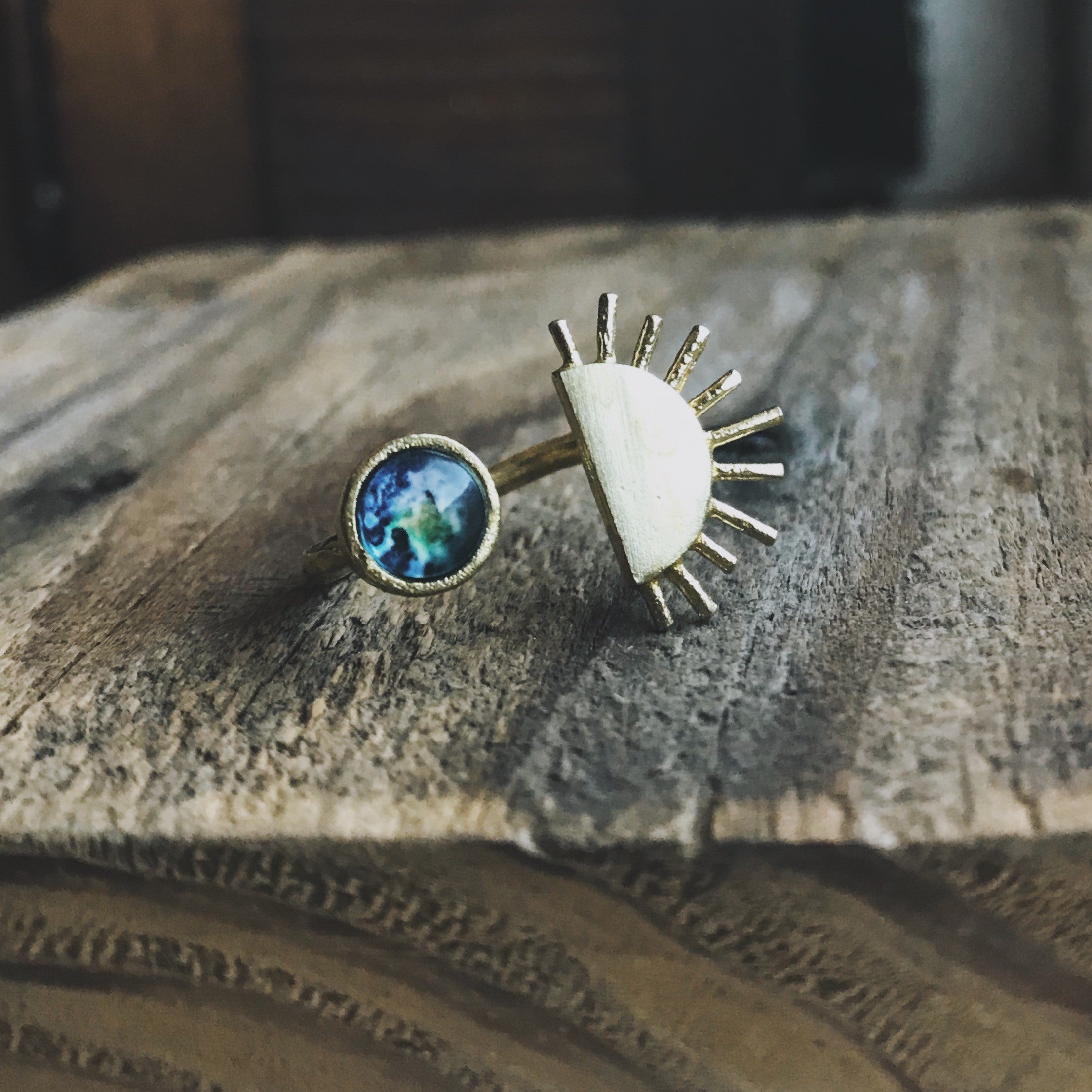 A hand embellished with two statement rings: one displaying the gold Sunrise Ring, the other featuring an Earth motif.