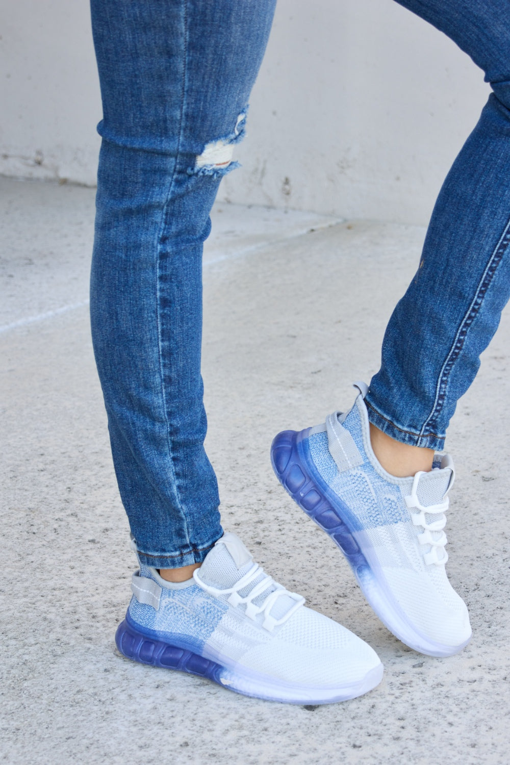 A person wearing distressed blue jeans and a pair of Forever Link Gradient Lace-Up Mesh Breathable Athletic Shoes, standing on a concrete surface.