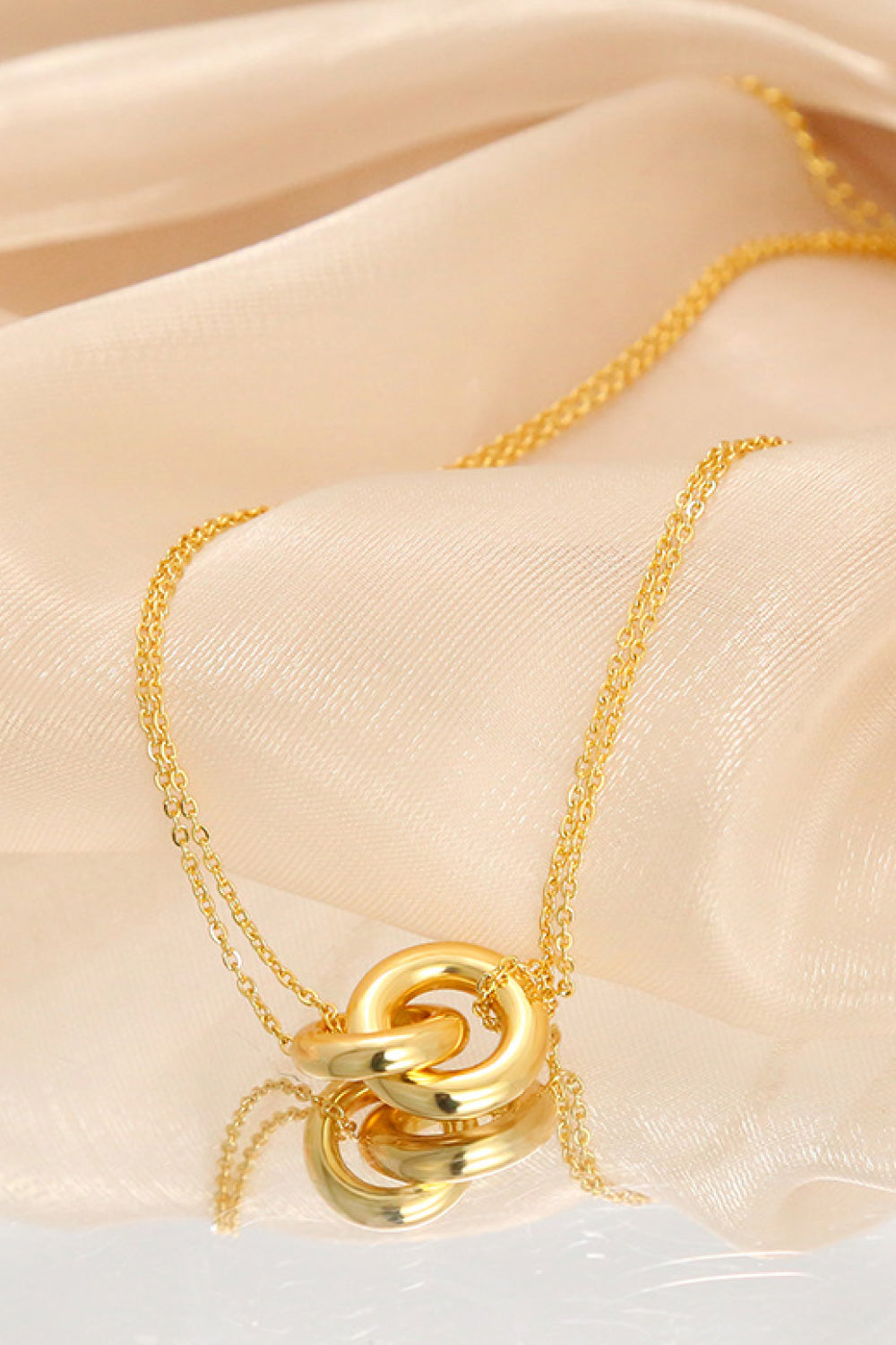 The Linked Ring Pendant Chain Necklace showcases an elegant design with a gold pendant featuring two interlocking circles.