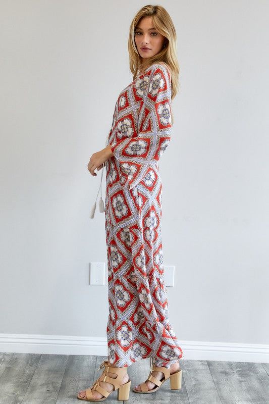 A person wearing a Printed Long Sleeve Loose Kimono with a bohemian blue and pink print over a white outfit stands in a room with a gray floor and white wall.