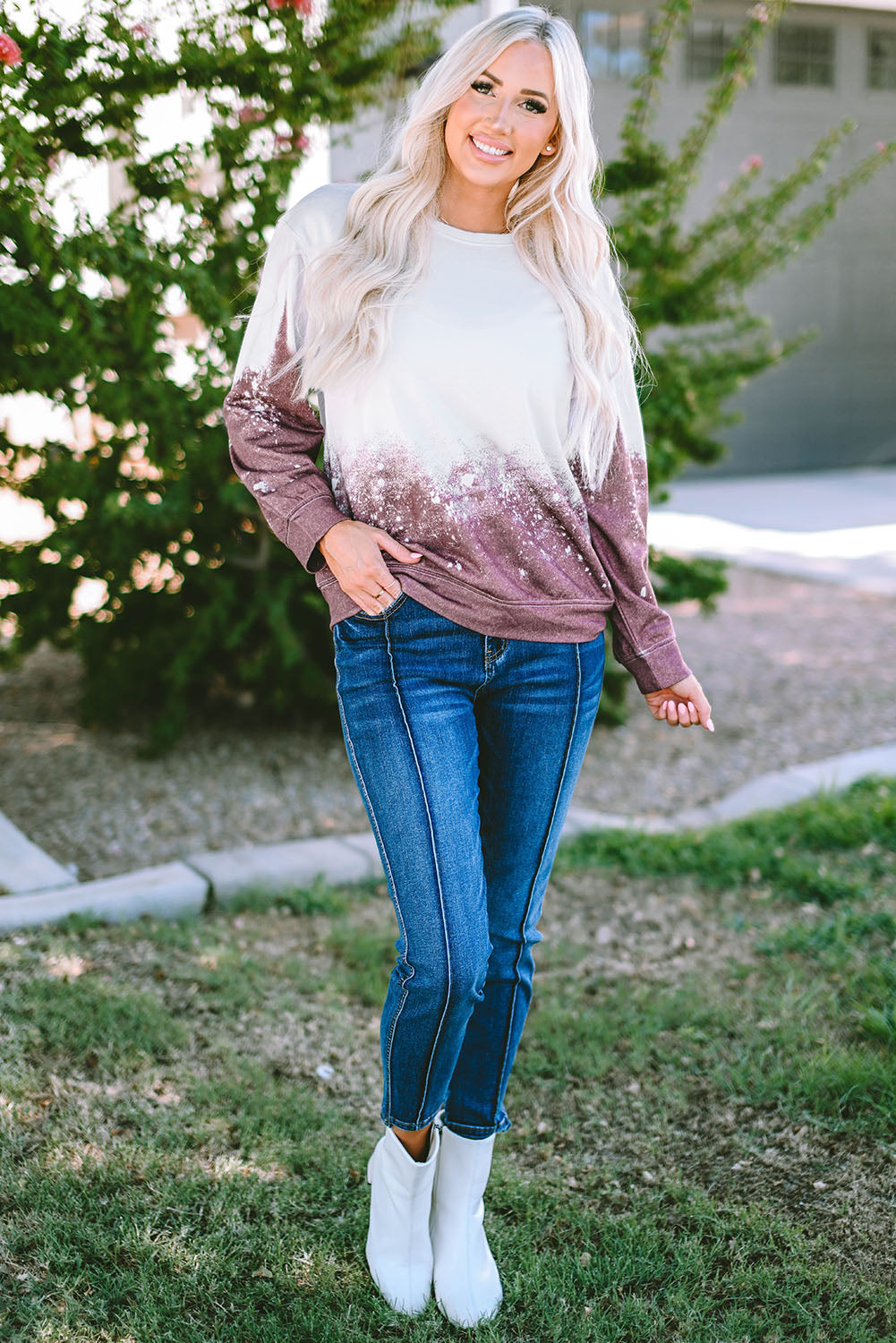 A person with long blonde hair is standing outdoors, facing away from the camera, wearing a Tie Dye Gradient Pullover Sweatshirt featuring a white and brown ombre splatter design.