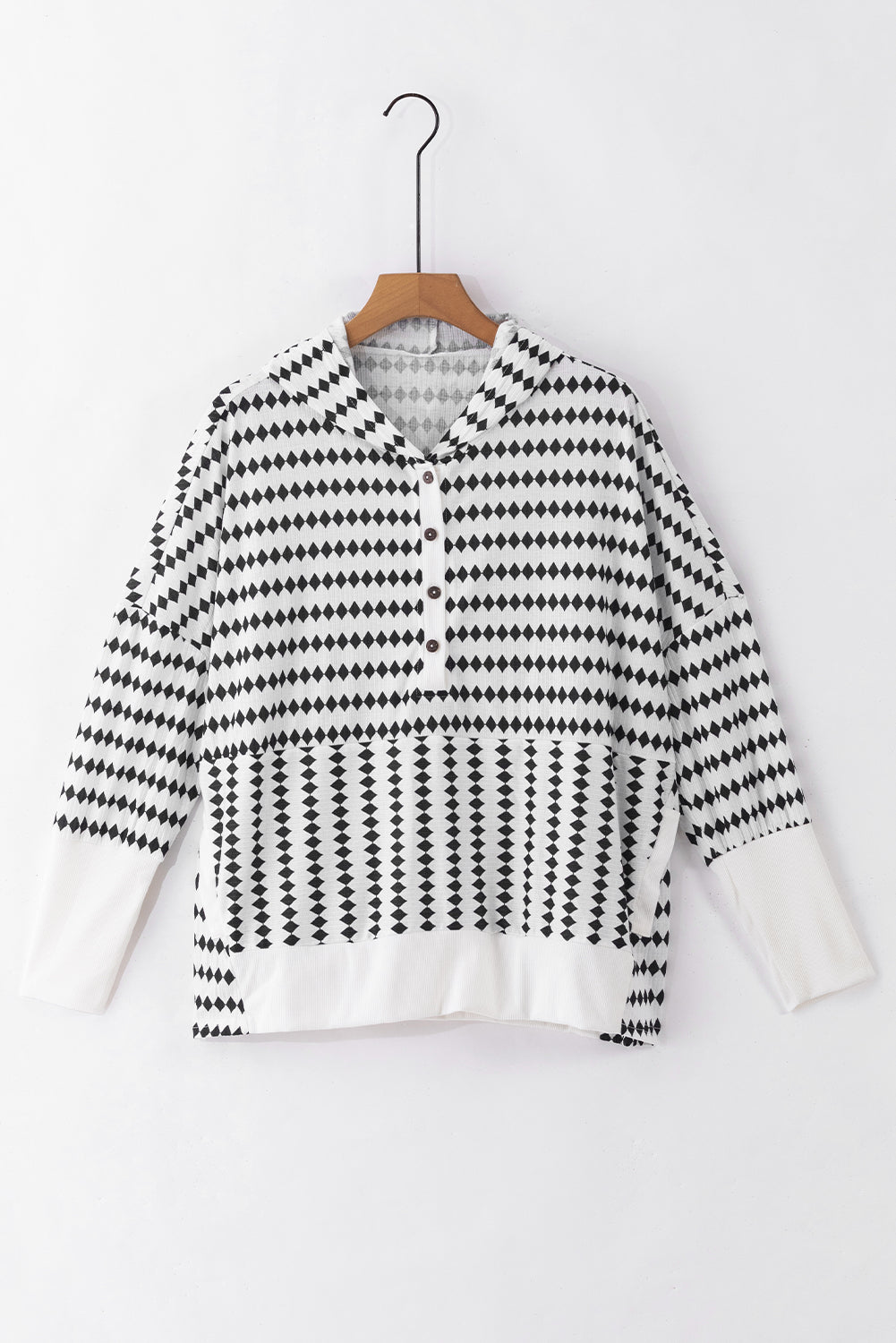 A woman in a Black Stripe Argyle Striped Half Button Oversized Hoodie stands in a room with light green brick walls, a painting of a sailboat, and a fan.