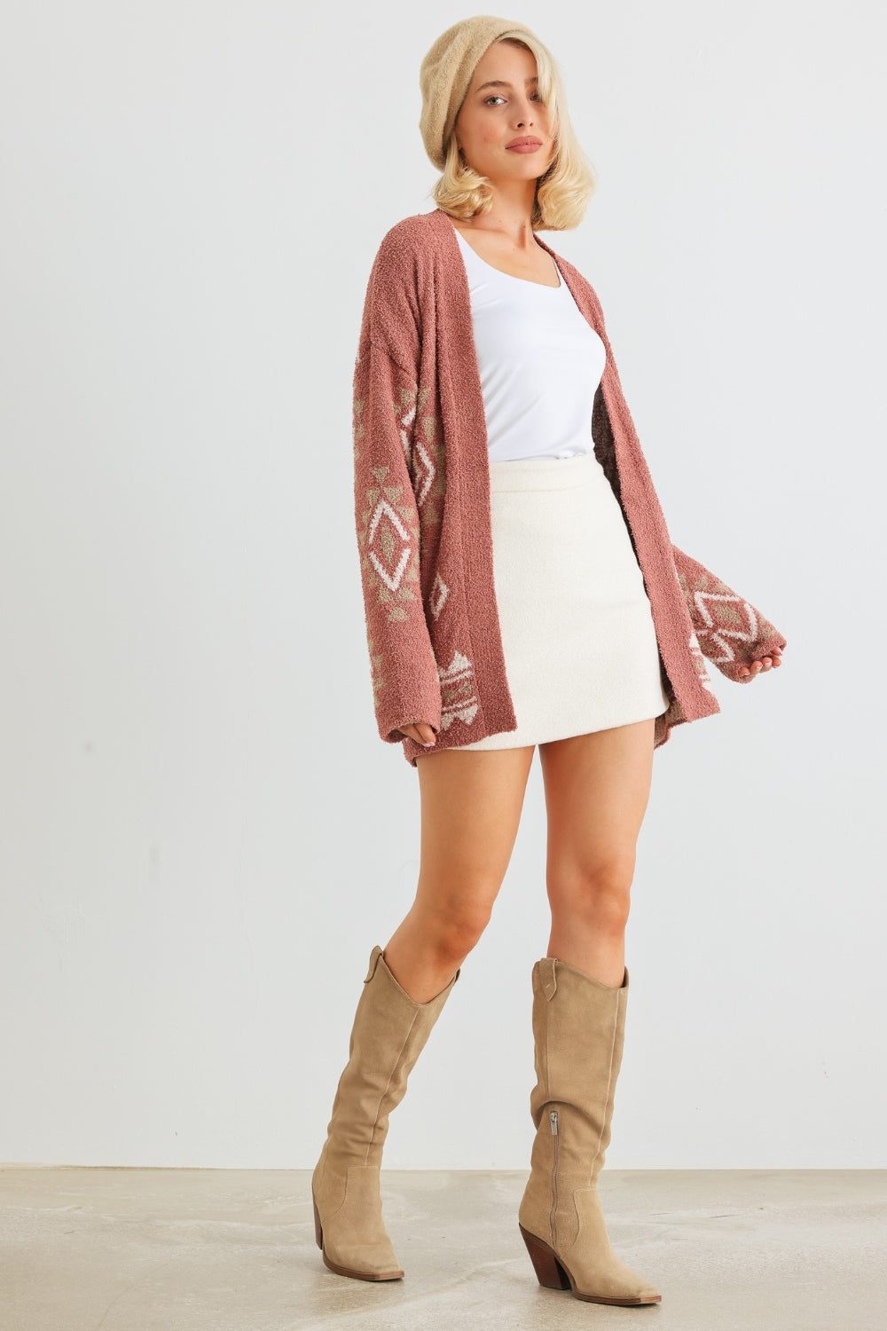 A woman wearing the VERY J/Loveriche Open Front Long Sleeve Cardigan in light pink—an absolute versatile wardrobe essential—paired with a white tank top, white skirt, and beige beret poses gracefully against a plain background.