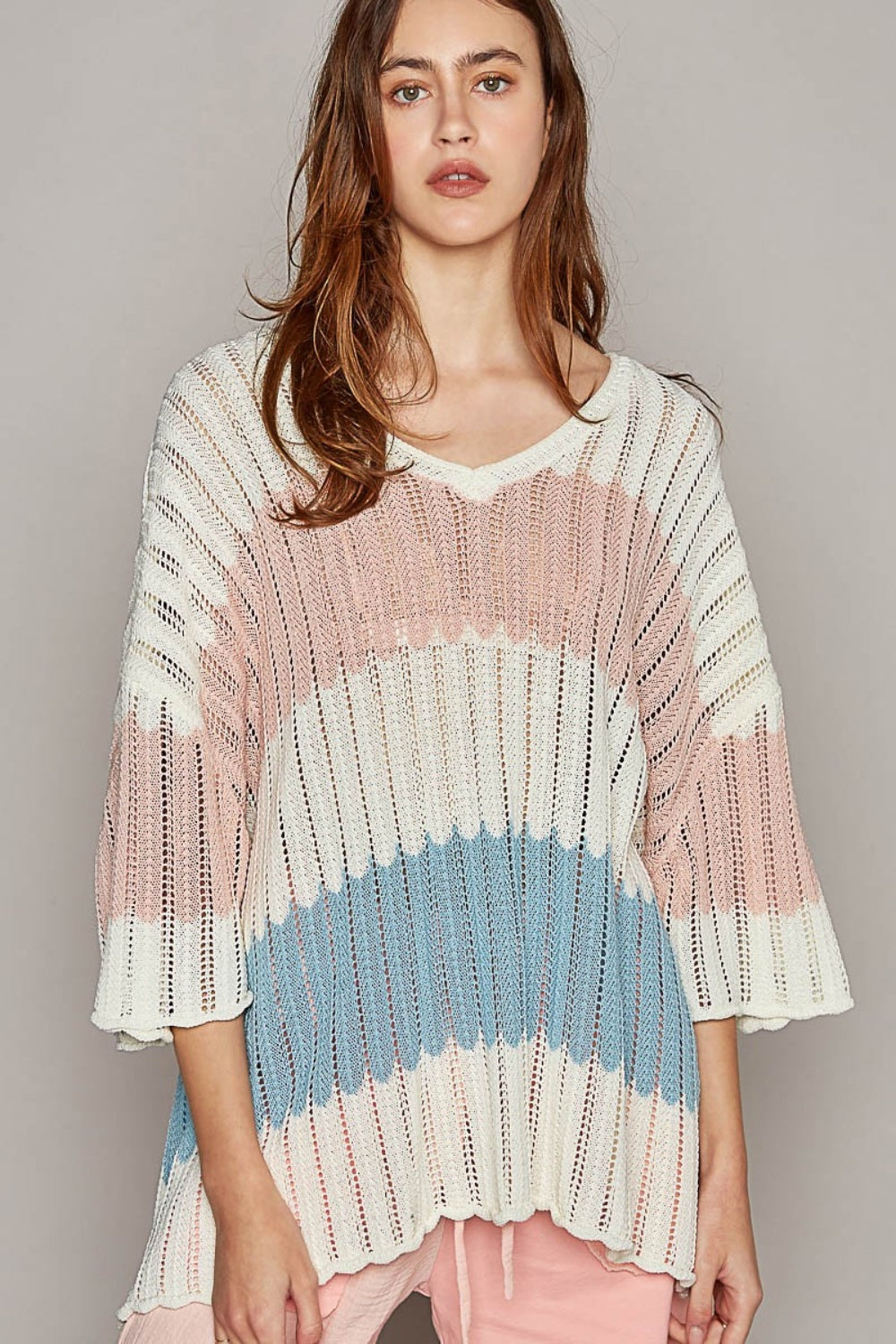 A woman with long hair wears a POL V-Neck Short Sleeve Stripe Weave Sweater featuring horizontal stripes in white, pink, and blue. She stands against a plain, light grey background.