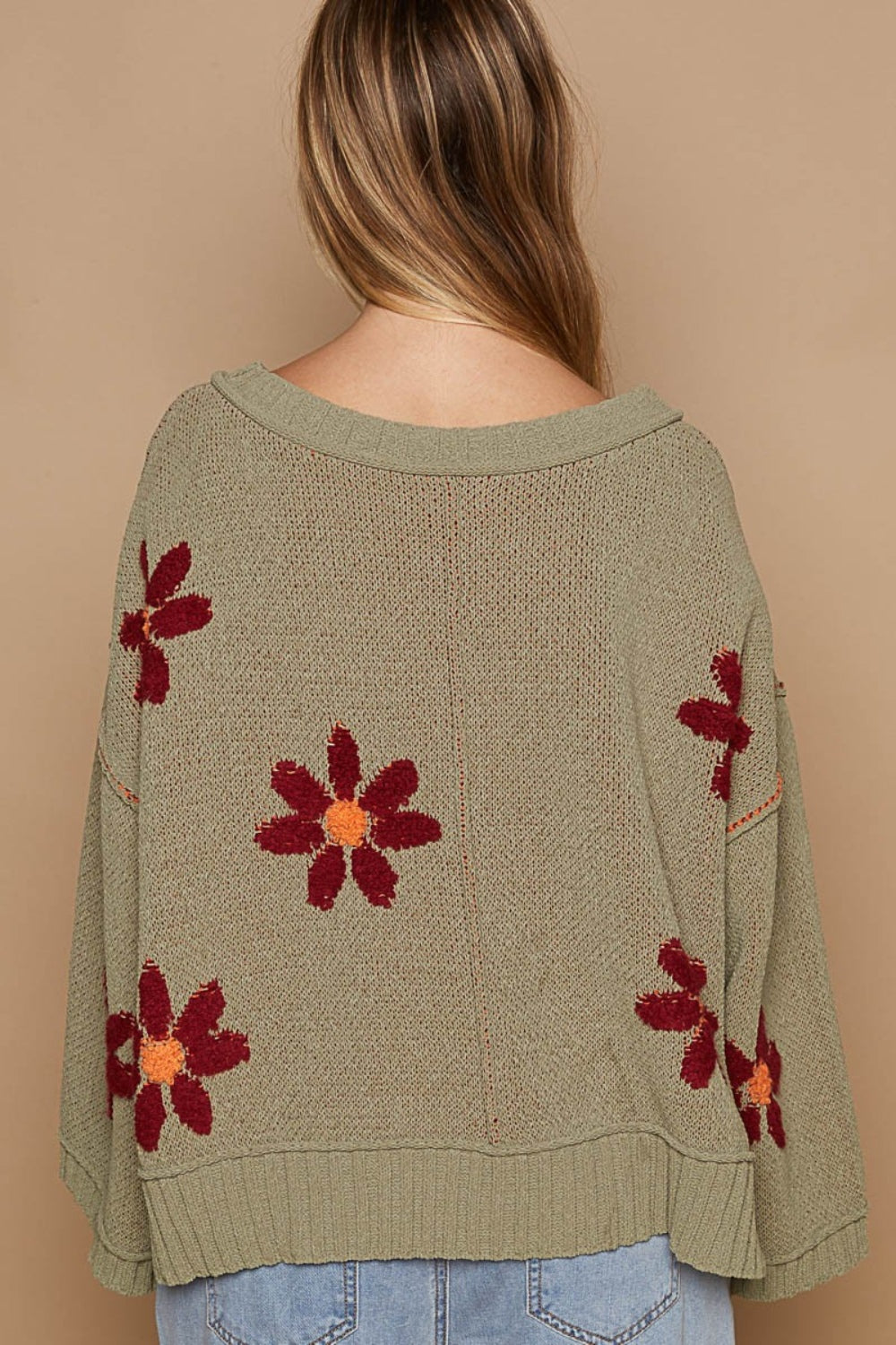 A person with curly hair wearing a fashionable outfit, featuring a POL V-Neck Floral Pattern Chenille Sweater in olive green adorned with red and orange flower patterns, is standing outdoors.