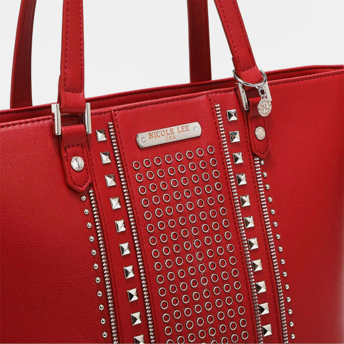 The Nicole Lee USA Studded Decor Tote Bag boasts a trendy appeal with its vegan leather material, highlighted by silver studs and dual shoulder straps, showcased against a white background.