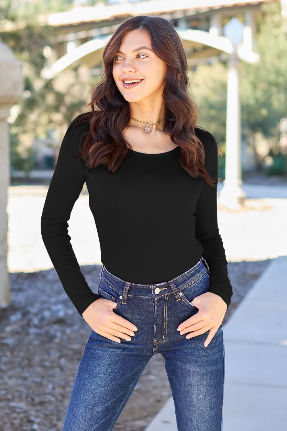 A person poses confidently in the Basic Bae Full Size Round Neck Long Sleeve Bodysuit, made from a rayon spandex blend, with one hand touching their neck and the other resting on their hip.