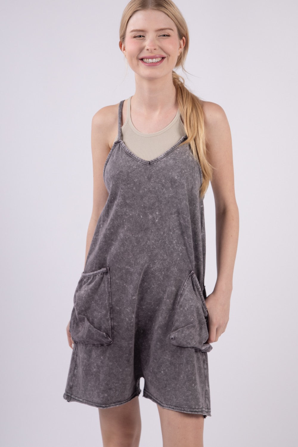 A person smiling against a plain background is wearing the VERY J V-Neck Sleeveless Washed Romper in gray, featuring two front pockets.