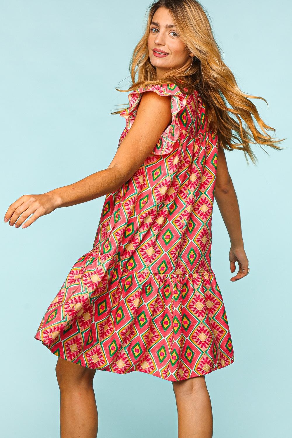 A woman with long hair smiles while wearing the fashionable and functional Haptics Full Size Ruffled Printed Dress with Side Pockets, featuring a geometric pattern, set against a light blue background.