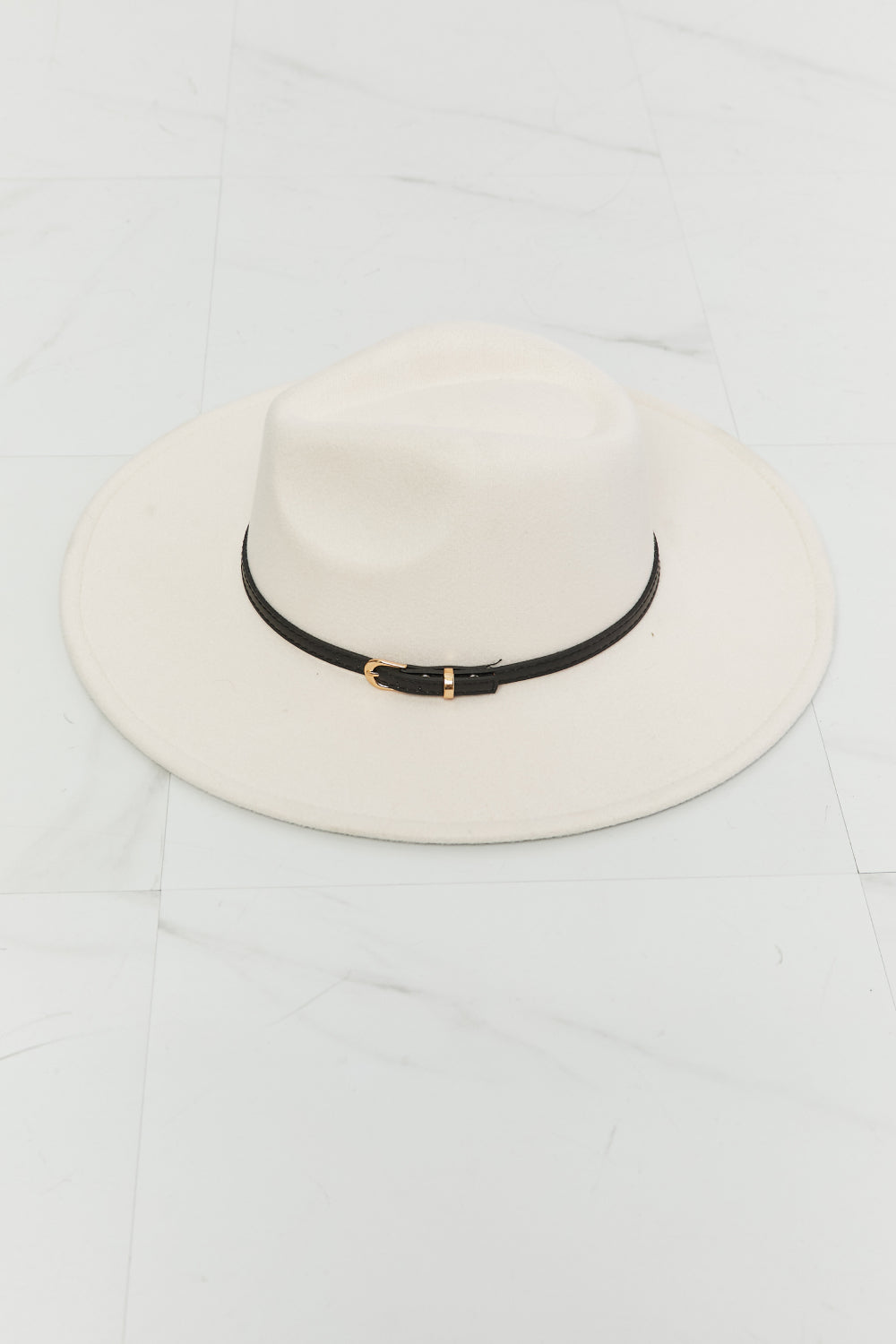 A person with long wavy hair wearing a white top and the Fame Keep It Classy Fedora Hat, which is beige with a black band, holding the brim of the hat with their hand.