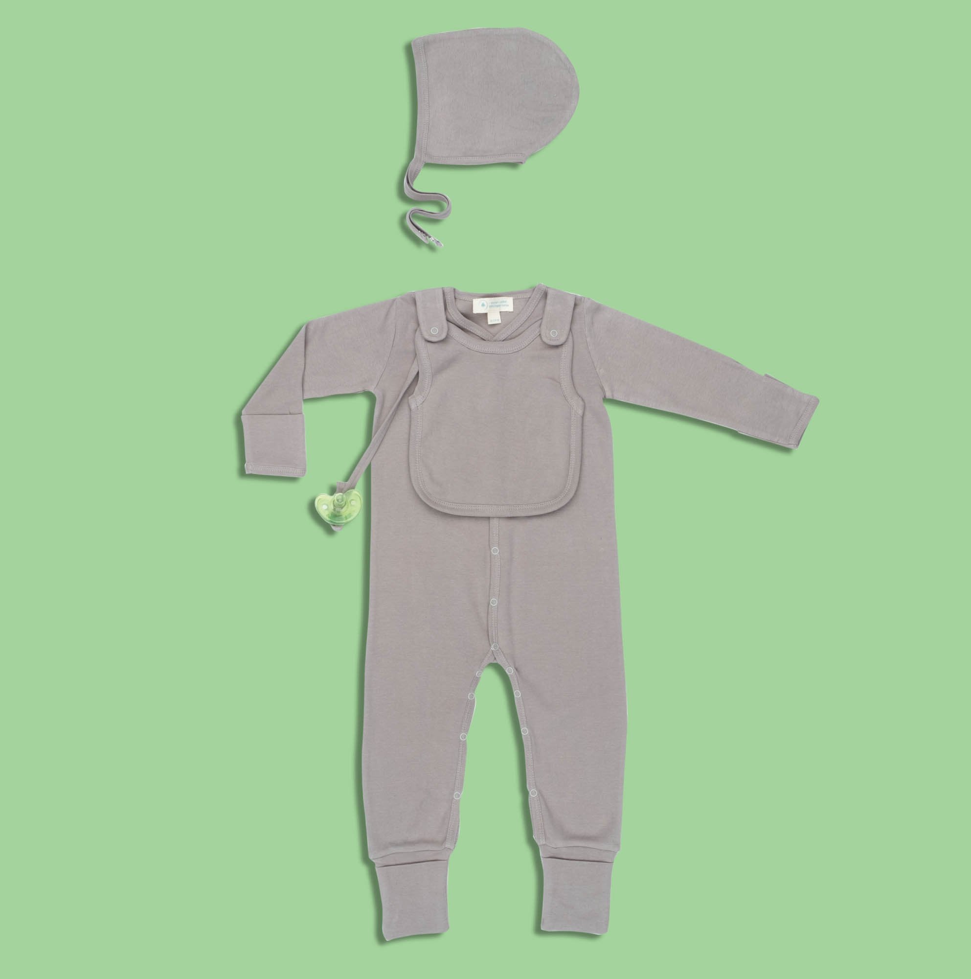 A baby is playing with the Smart Footed One-Piece + Bib - Gray by Fuchsia Milo in a living room.