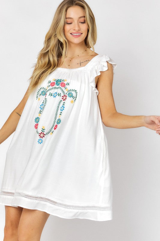 A woman in an Embroidered Square Neck Mini Dress, featuring a coral hue, stands near plants adjusting her hair—the perfect summer attire.