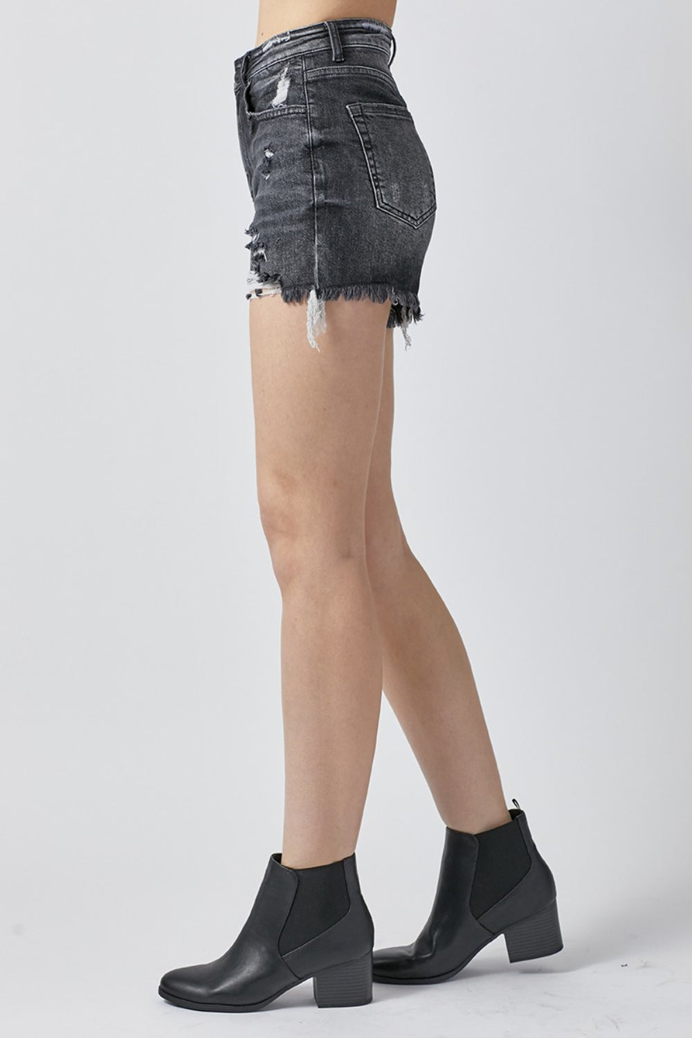 A person wearing RISEN Full Size High Rise Distressed Denim Shorts stands against a plain background, making a stylish addition to any summer wardrobe.