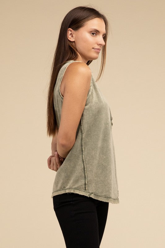 A woman with long brown hair is wearing the Washed Half-Button Raw Edge Sleeveless Henley Top in green and black pants, standing against a beige background.