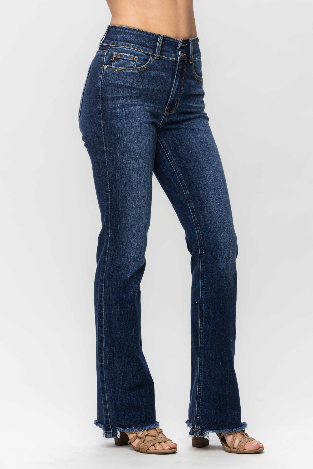 A person wearing trendy and stylish Judy Blue Full Size Frayed Hem Bootcut Jeans with a distressed finish and open-toed sandals is standing against a plain white background.