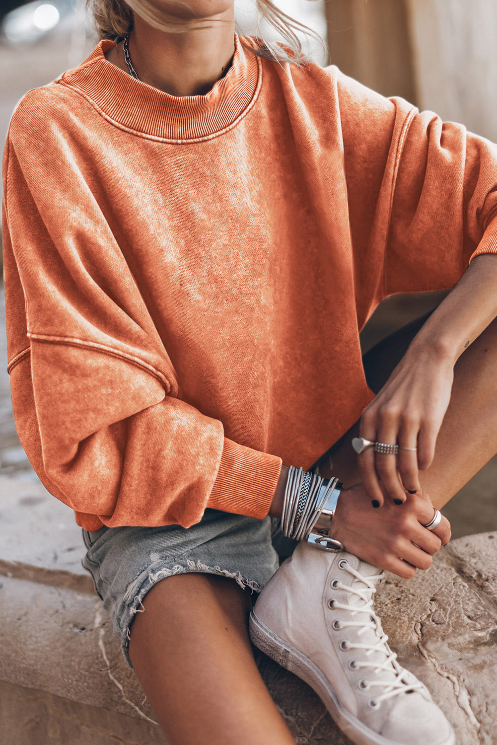 A person with long blonde hair wearing an Orange Drop Shoulder Crew Neck Pullover Sweatshirt and blue jeans stands with their back to the camera in a sunflower field.