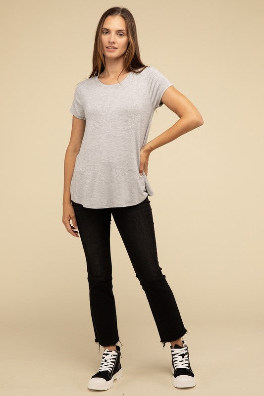 A person with long hair is wearing a blue Flowy Round Hem Rayon Short Sleeve Top and black pants, standing against a plain beige background.