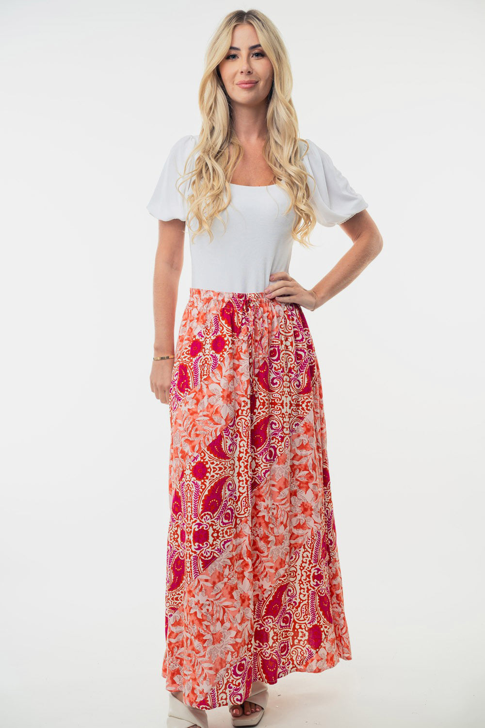 A woman stands posing against a white background, wearing a white short-sleeved blouse paired with the White Birch Full Size High Waisted Floral Woven Skirt, which showcases colorful patterns. The outfit creates a flattering silhouette perfect for any occasion.