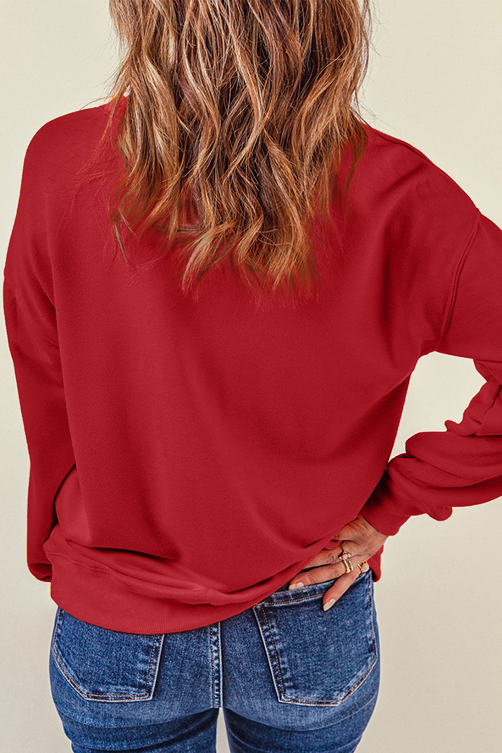 A person wearing a long-sleeved red shirt and blue jeans stands with their back to the camera, one hand resting on their hip, as if showcasing a cozy Fiery Red Plain Crew Neck Pullover Sweatshirt for winter.