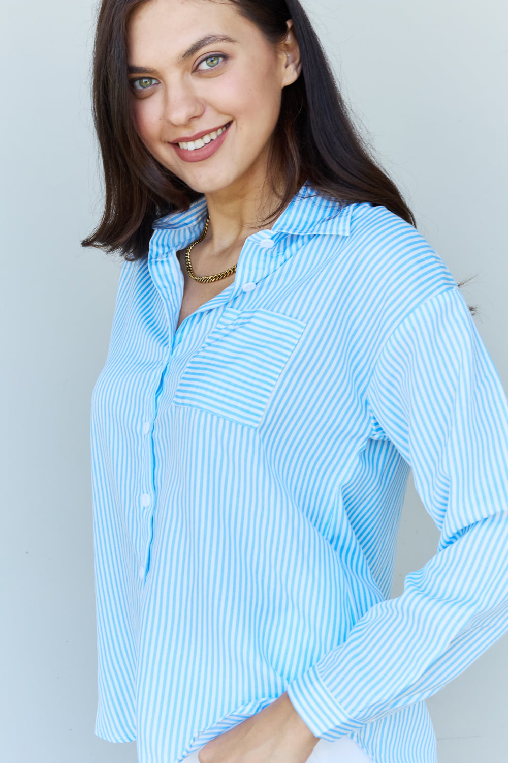 A person with long dark hair smiles while wearing the Doublju She Means Business Striped Button Down Shirt Top in light blue and white shorts, standing against a plain light background.