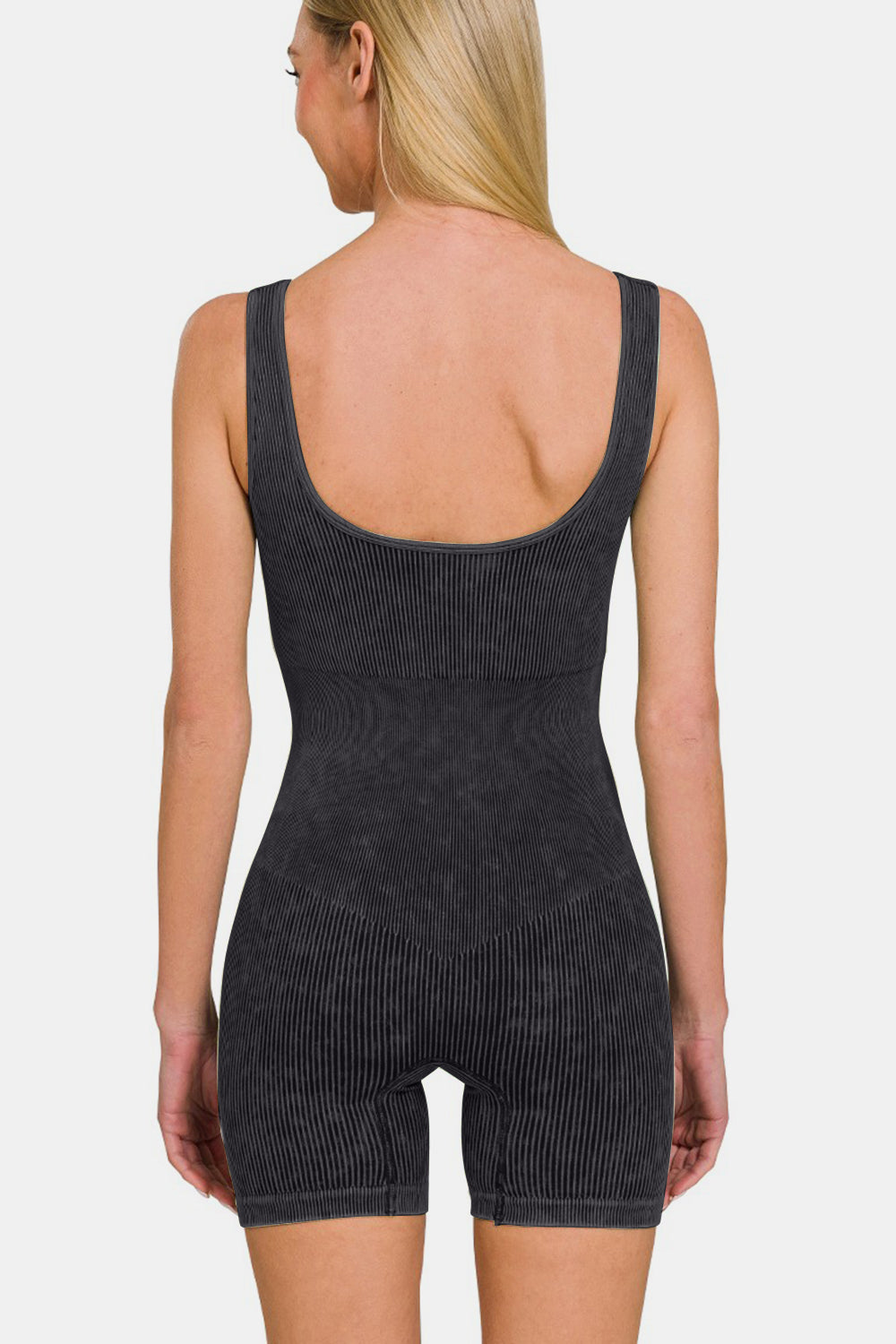 A person with long blonde hair sporting a versatile piece, the Zenana Washed Ribbed Romper with Pad, stands with one hand on their hip against a plain background.