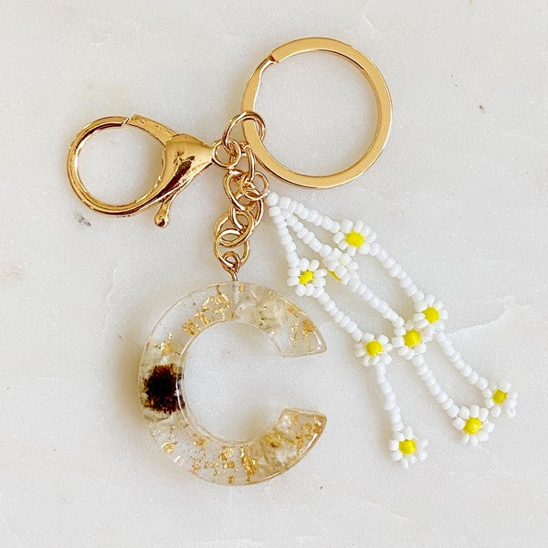 Baby Daisy Initial Key Chain alphabet keychains with real daisy flowers and gold flakes on a marble surface.