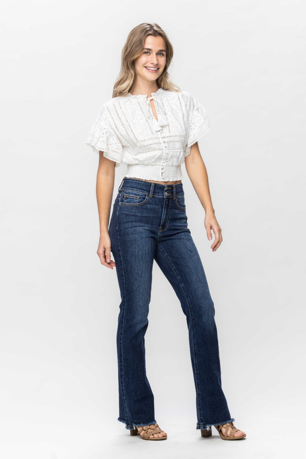 A person wearing trendy and stylish Judy Blue Full Size Frayed Hem Bootcut Jeans with a distressed finish and open-toed sandals is standing against a plain white background.