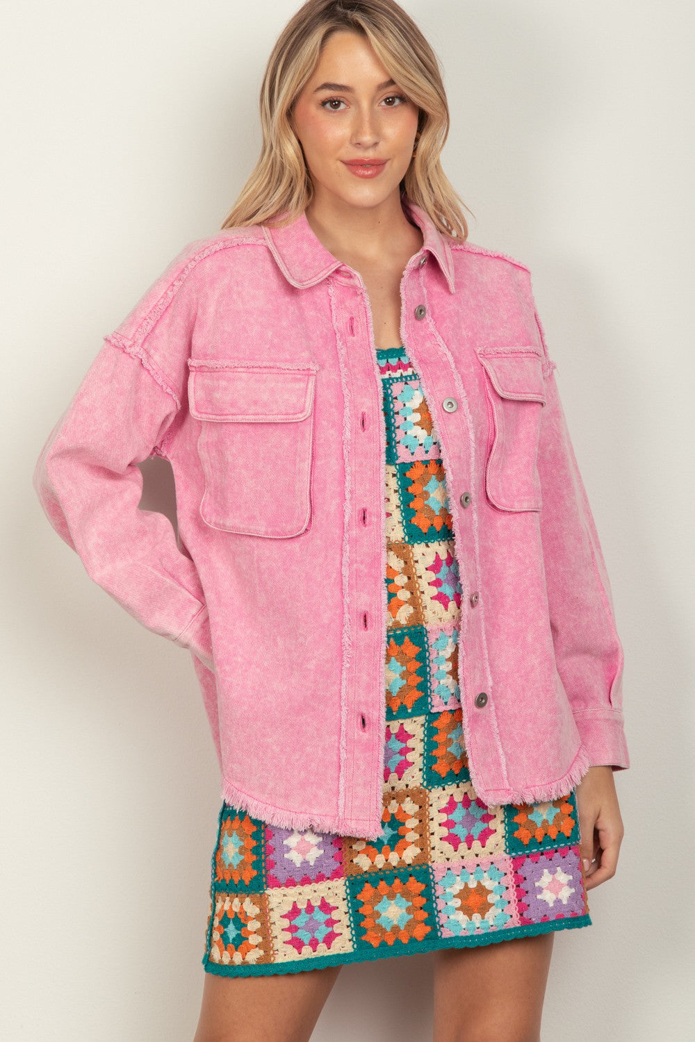 Person wearing a VERY J Full Size Button Up Raw Hem Long Sleeve Jacket in pink over a colorful, patterned dress, standing against a plain background.