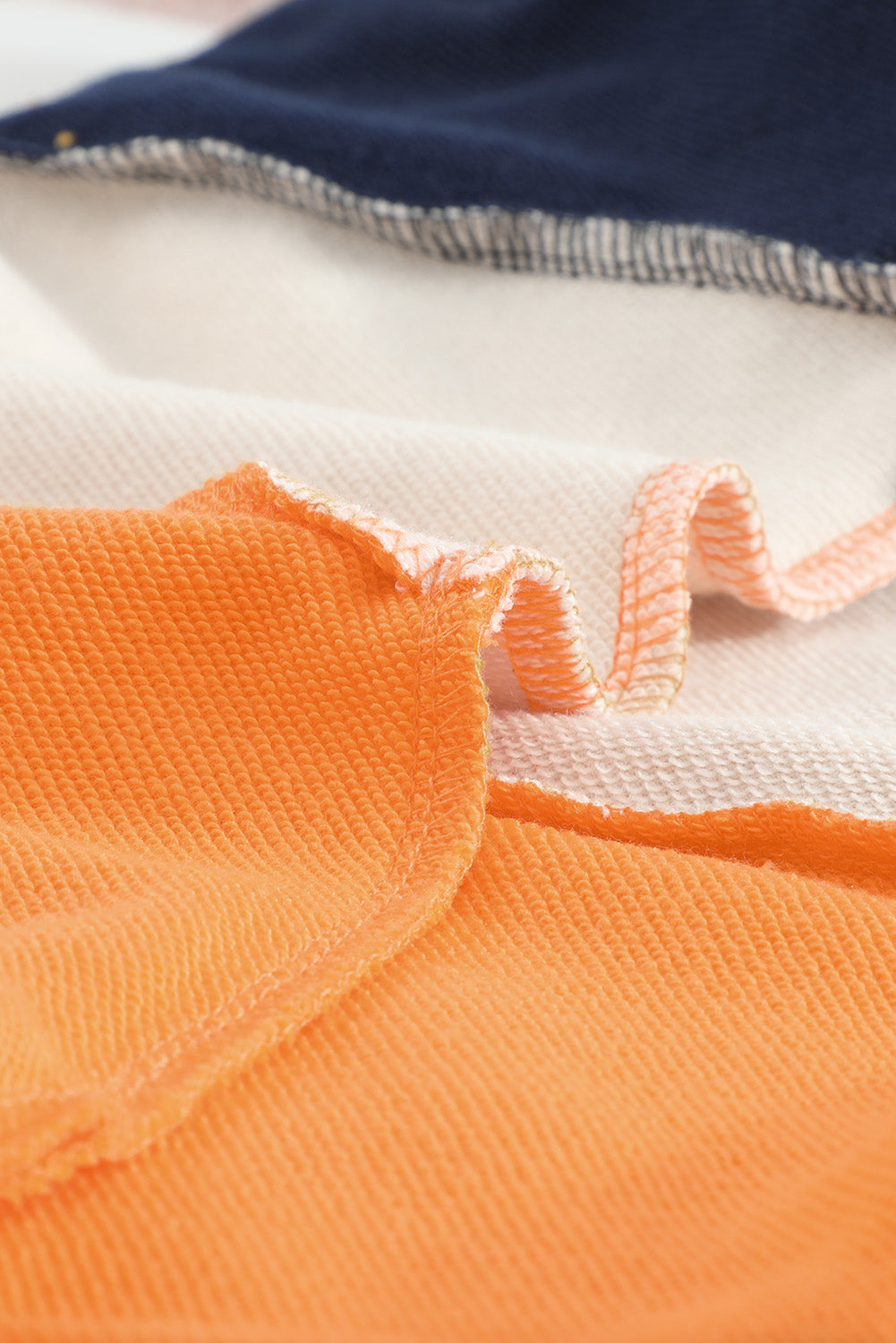 Person with wavy, shoulder-length hair wearing a Colorblock Orange Contrast Stitching Sweatshirt with Slits, paired with blue skinny fit jeans, standing with back to the camera against a gray textured wall.