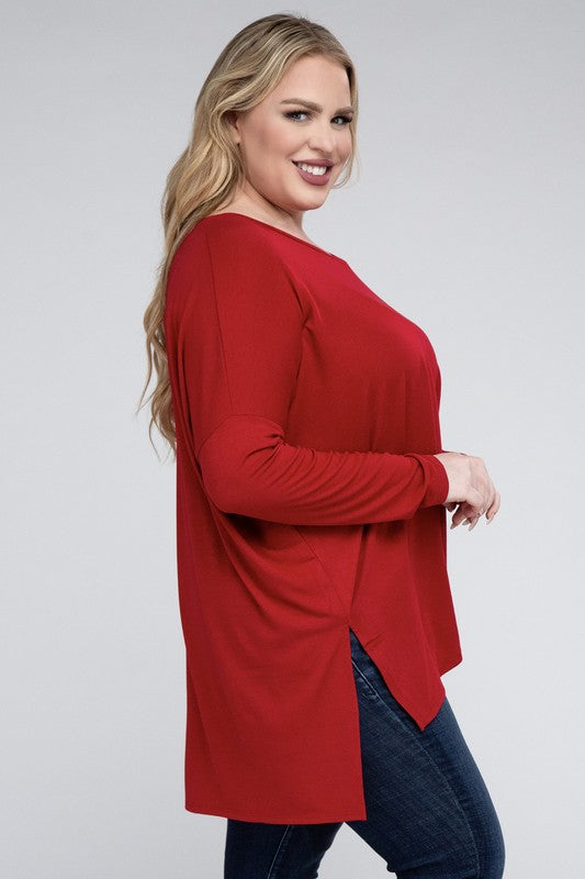 A woman with long, blonde hair wears a Plus Dolman Sleeve V-Neck Side Slit Hi-Low Hem Top and blue jeans, posing with one hand on her hip and smiling at the camera.