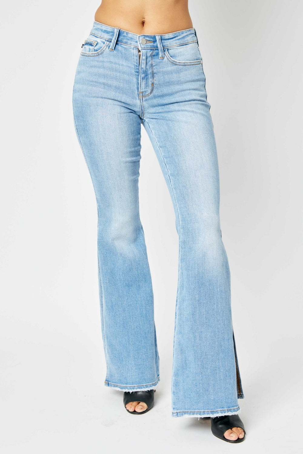 A person is wearing Judy Blue Full Size Mid Rise Raw Hem Slit Flare Jeans with a flattering silhouette and black open-toe shoes.