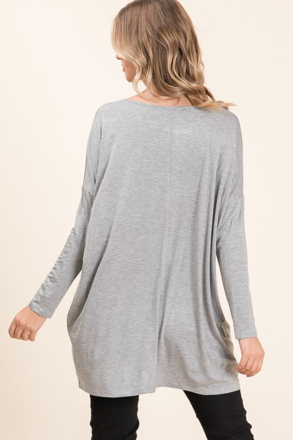 A woman is smiling and posing in the versatile and comfortable BOMBOM Round Neck Long Sleeve Oversized Top, paired with black pants, against a neutral background.