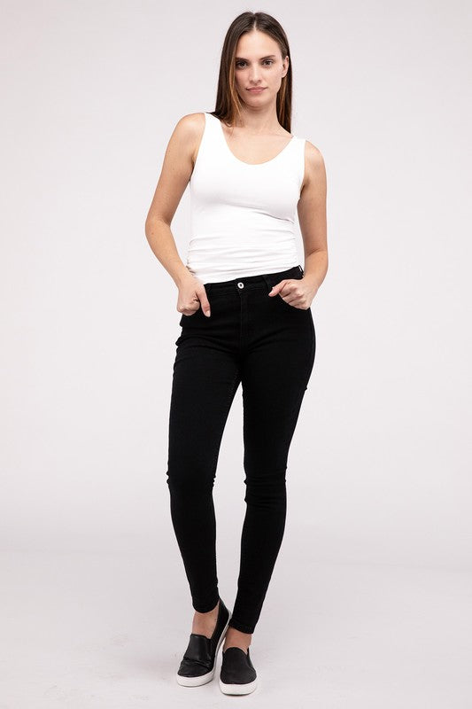 A woman in a white Front & Back 2-Way V-Neck Seamless Tank and black pants, standing with hands on hips and looking at the camera.