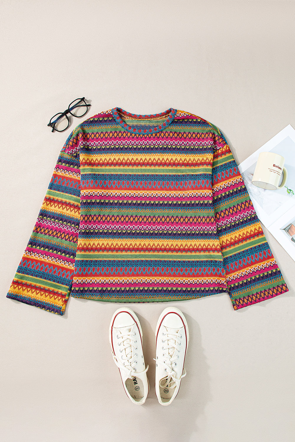 A person stands with hands in the pockets of their denim shorts, wearing a colorful Rose Red Ethnic Wavy Pattern Drop Shoulder Knit Top and a white shoulder bag.