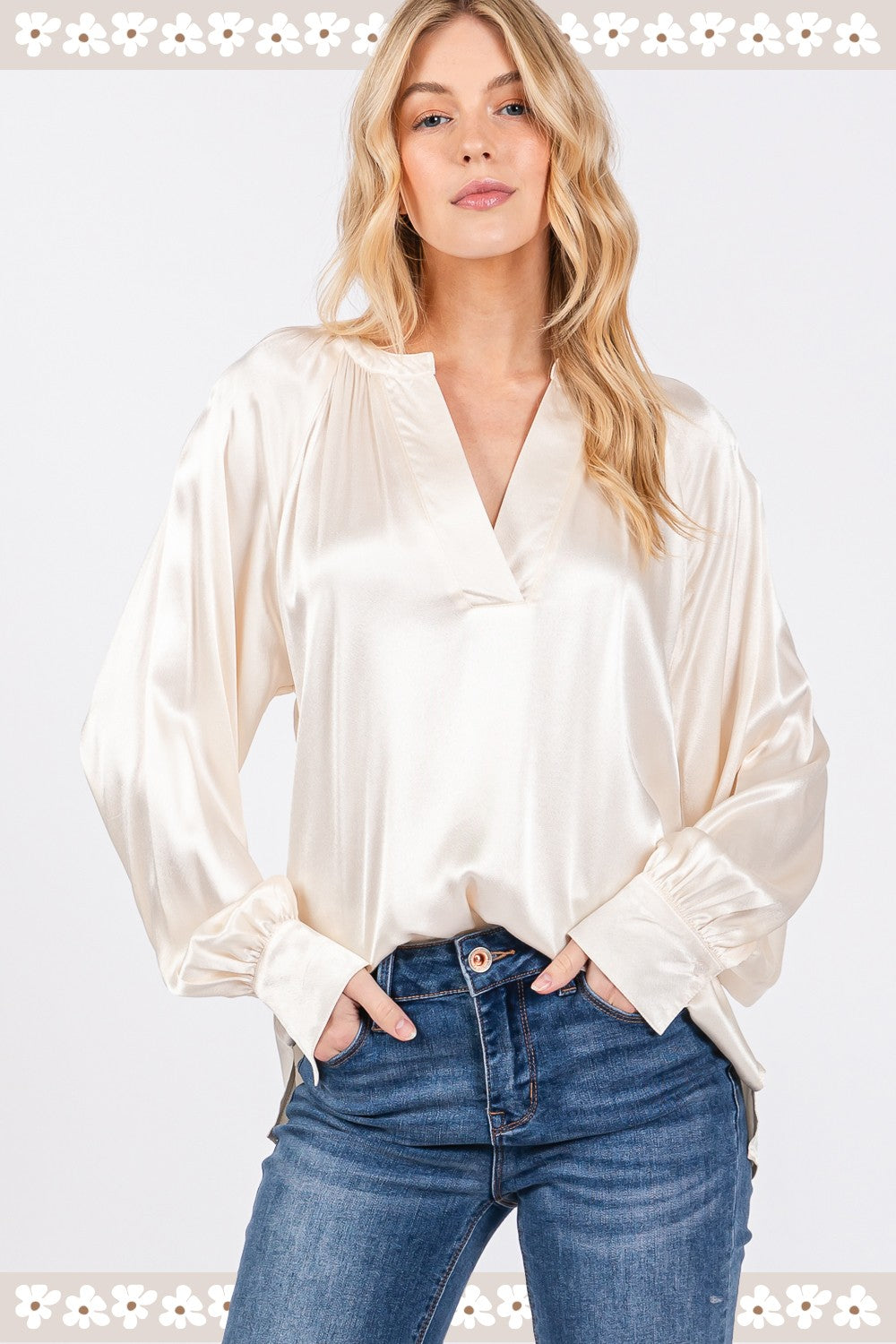 A person is wearing a SAGE + FIG Notched Long Sleeve Blouse in cream-colored satin paired with blue jeans.