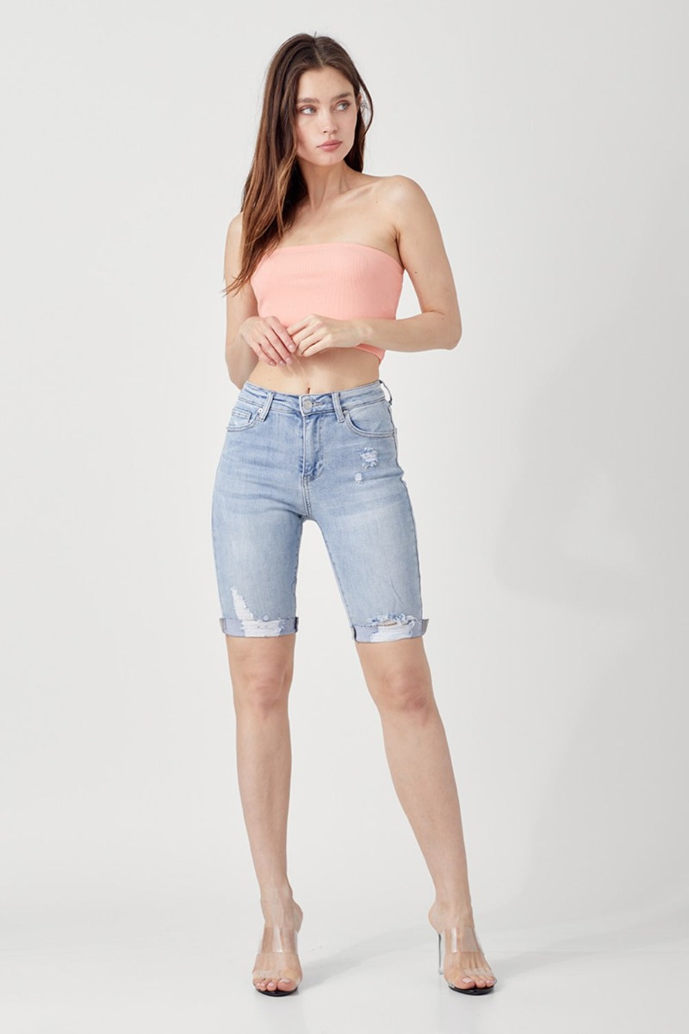 Person wearing RISEN High Rise Distressed Denim Bermuda Shorts with rolled cuffs, showcasing a flattering silhouette against a plain background—giving a trendy twist to classic denim.