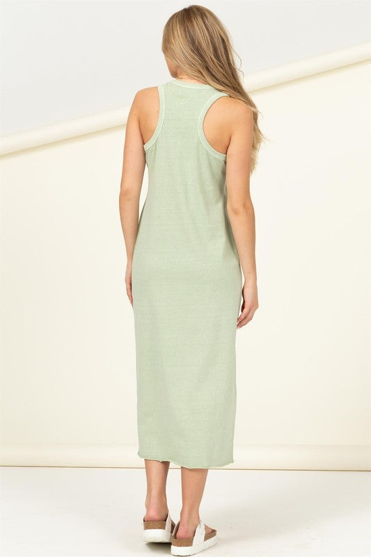 A woman dressed in a Fun Day Sleeveless Shift Midi Dress, light green and ankle-length, stands against a light background. She pairs the outfit with white sandals and a necklace.