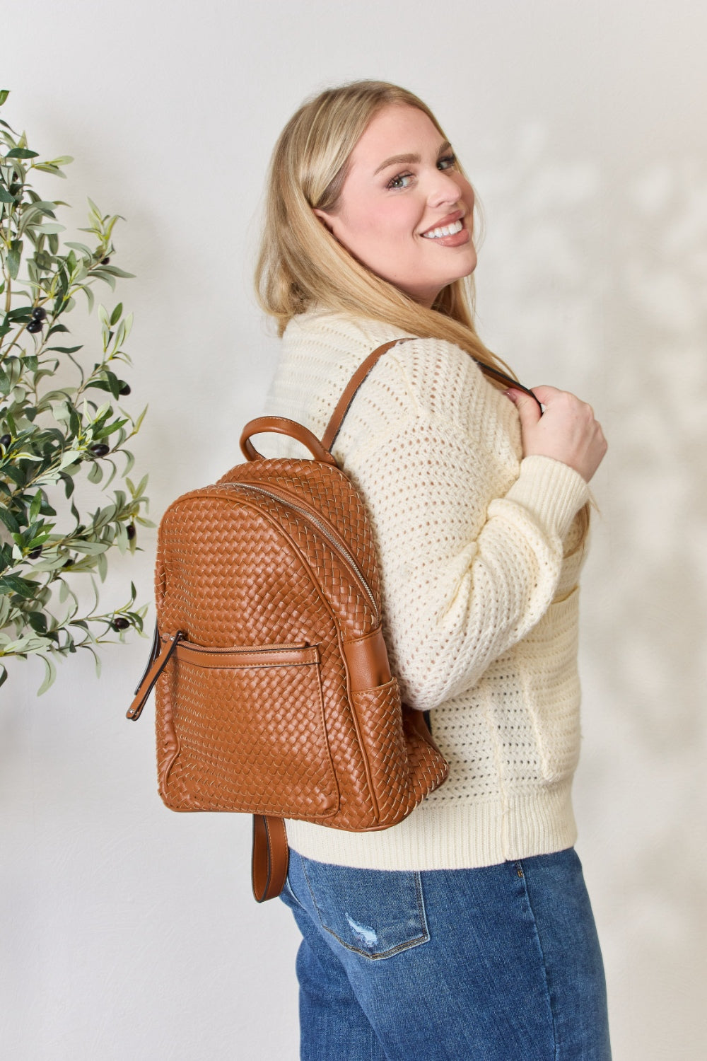 A person wearing a cream sweater and blue jeans carries the SHOMICO PU Leather Woven Backpack, showcasing exquisite craftsmanship with its woven design.