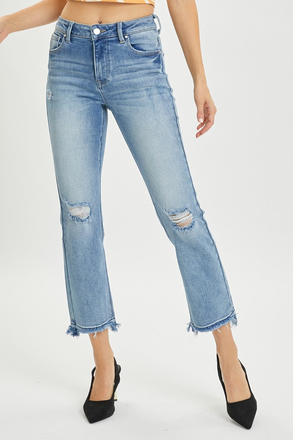 A person wearing the RISEN Full Size High Rise Distressed Cropped Straight Jeans in light blue with frayed hems, paired with black pointed-toe heels.
