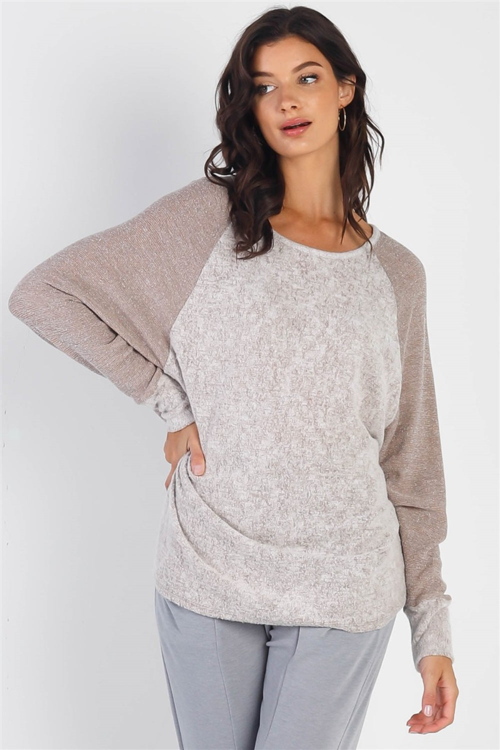 A woman stands wearing the Cherish Apparel Round Neck Long Sleeve Contrast Top in pink and gray with matching gray pants, set against a plain background.