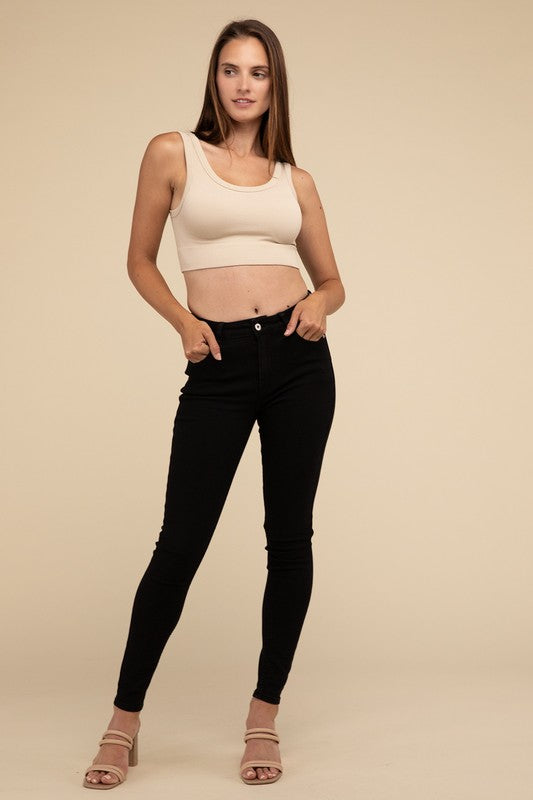 A person with long brown hair wearing the Ribbed Seamless Crop Top in light blue and black pants stands against a beige background, showcasing a perfect summer essential.