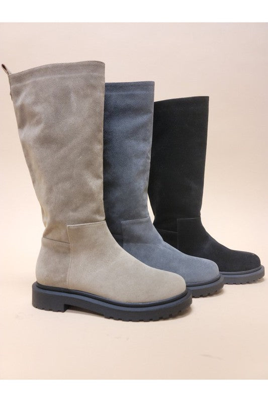 Three pairs of UNA-LONG BOOTS in beige, grey, and black are aligned in a row against a neutral background. These casual suede long boots feature chunky rubber soles and block heels.