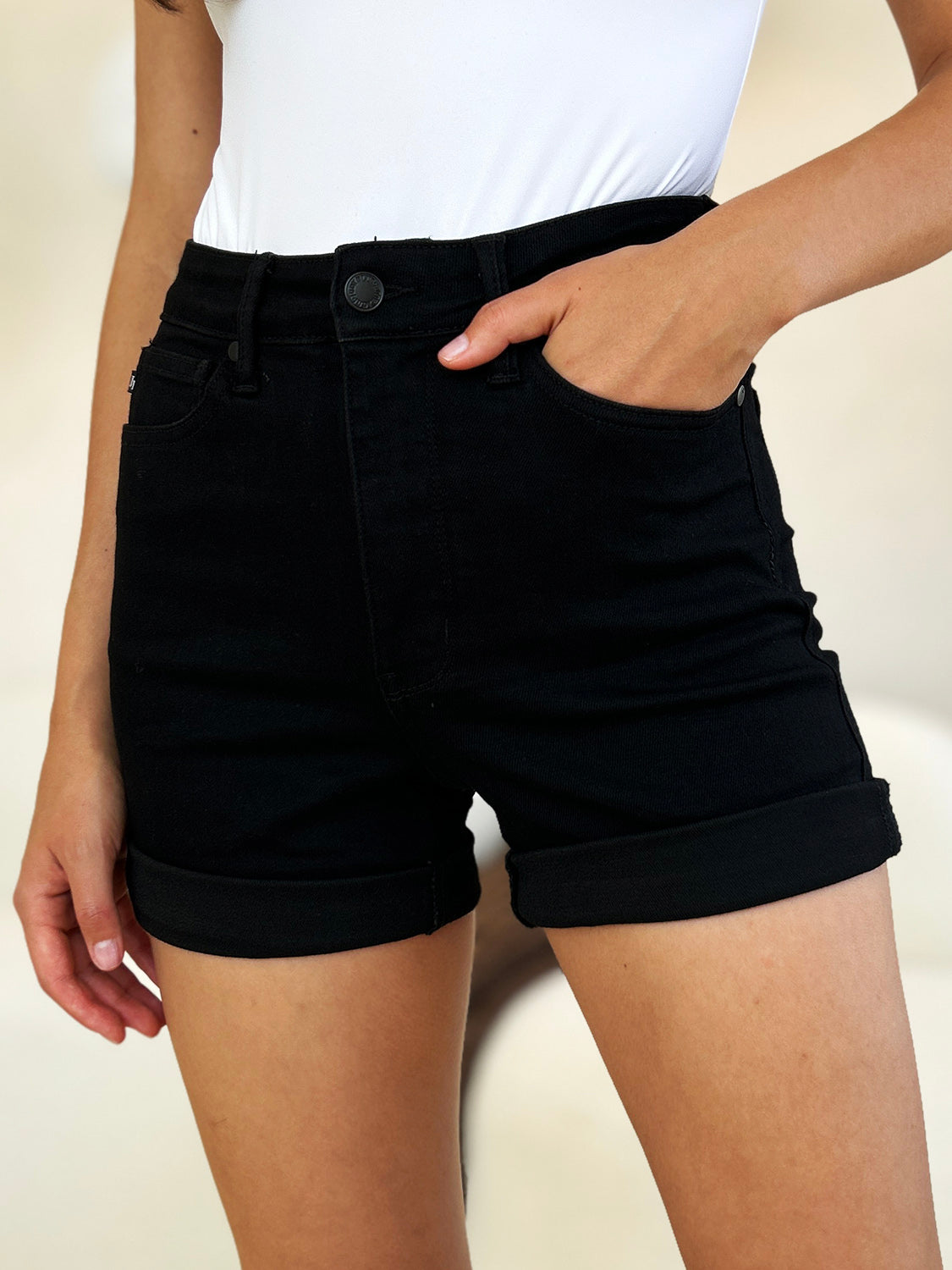 Person wearing a white top and Judy Blue Full Size High Waist Tummy Control Cuffed Denim Shorts, one hand in pocket.