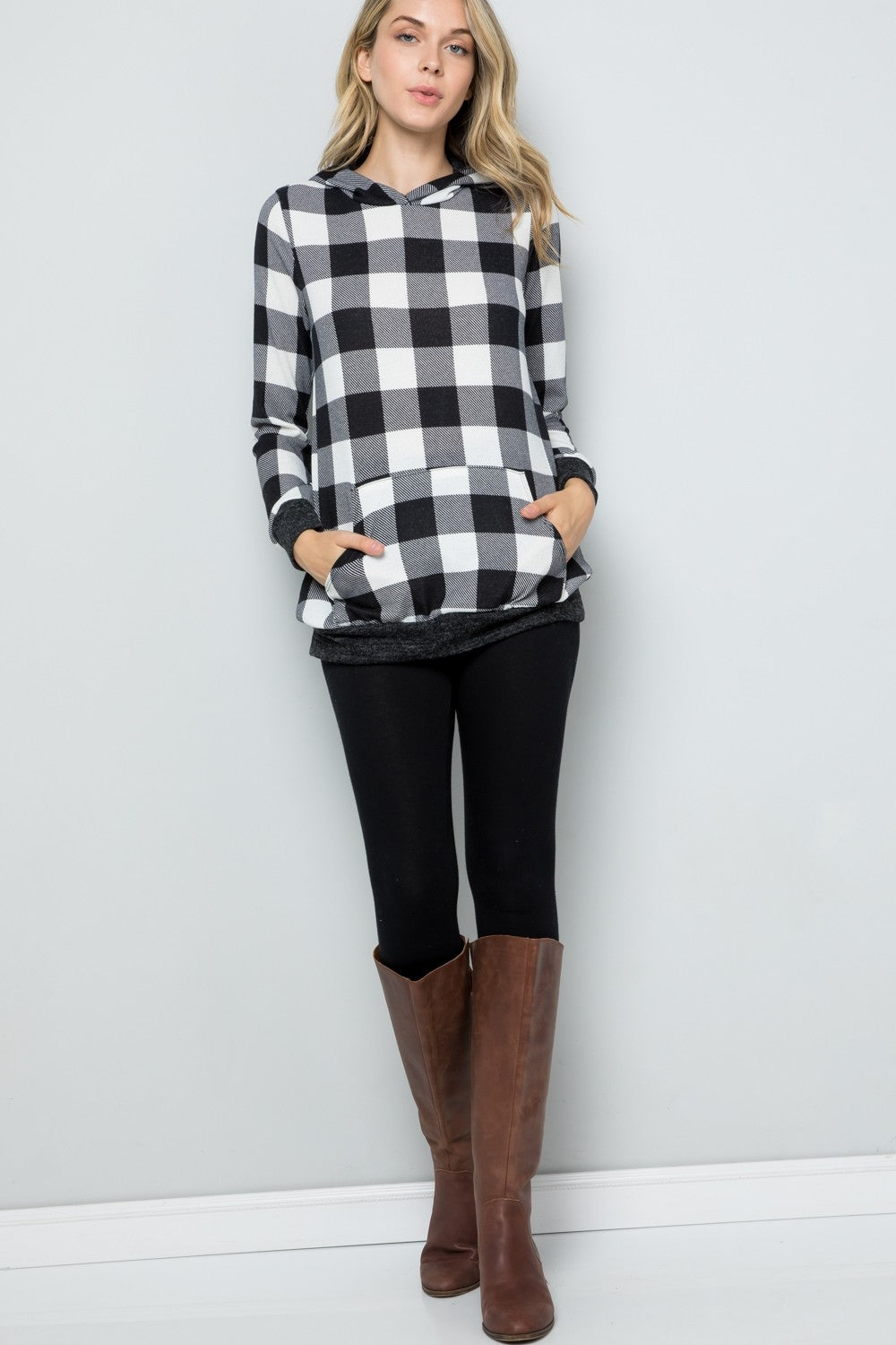 A woman wearing the Celeste Full Size Contrast Plaid Long Sleeve Hoodie smiles while standing against a plain background, showcasing her casual wardrobe.