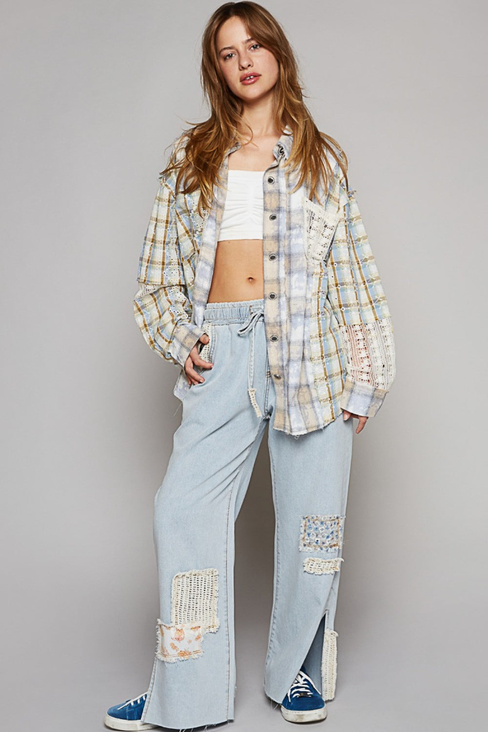 A young woman poses against a plain background, wearing the POL Long Sleeve Embroidered Crochet Plaid Shirt over a white crop top and drawstring light-blue pants.