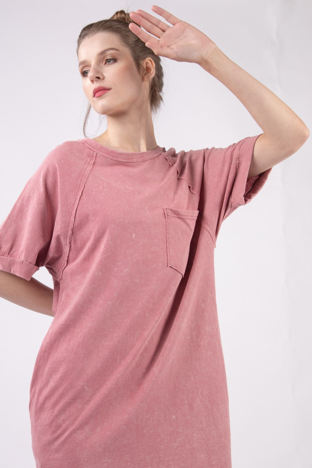 Wearing the VERY J Washed Round Neck Mini Tee Dress in pink, a person stands sideways against a plain background, effortlessly showcasing their casual wardrobe style.