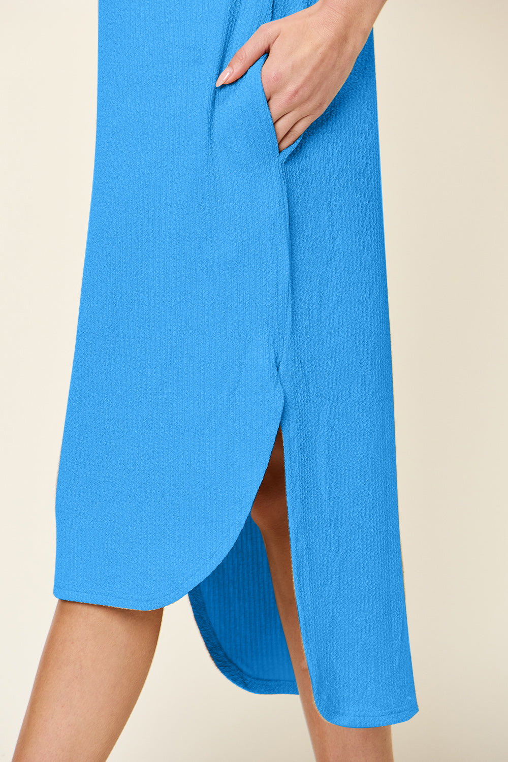 A person in a blue Double Take Full Size Round Neck Short Sleeve Slit Dress, made from a comfortable polyester-spandex blend, stands against a neutral background, wearing black sandals and minimal accessories.