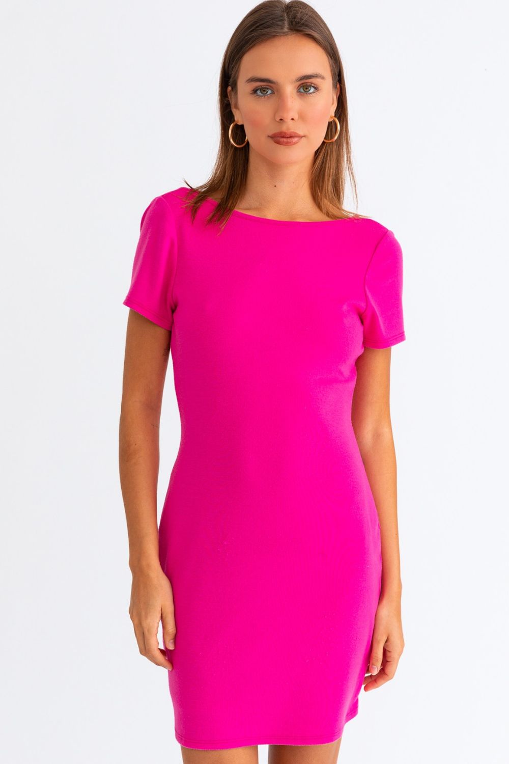 A person stands against a plain white background, wearing the Le Lis Short Sleeve Low Back Mini Dress in bright pink.