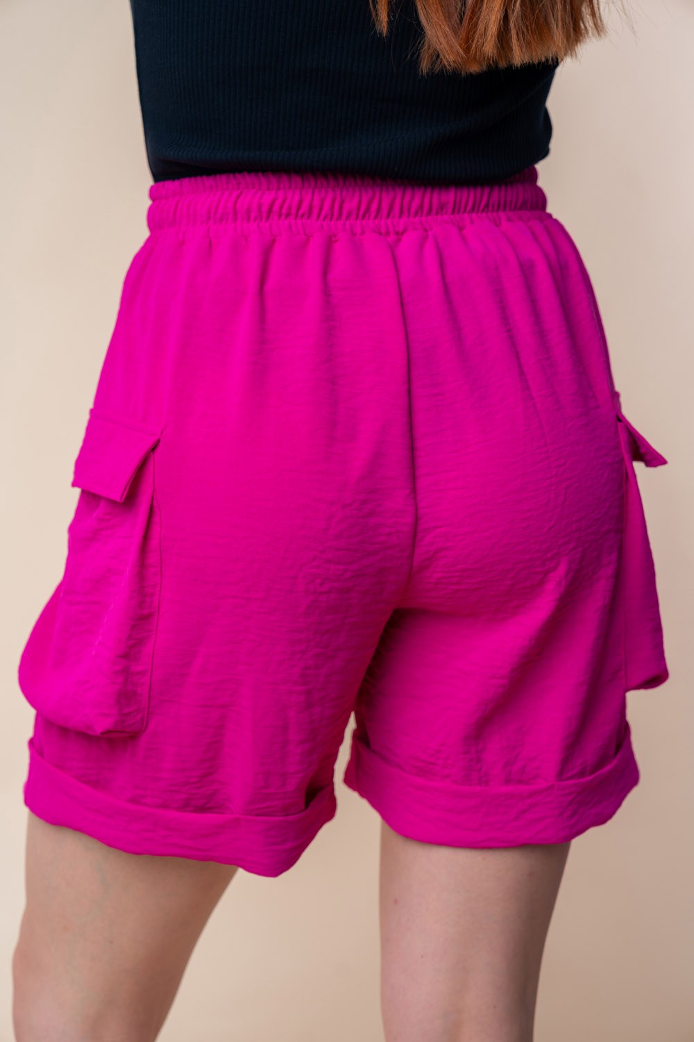 A person is wearing the White Birch High Waisted Drawstring Knit Cargo Shorts in bright pink, featuring side pockets and a drawstring waistband.